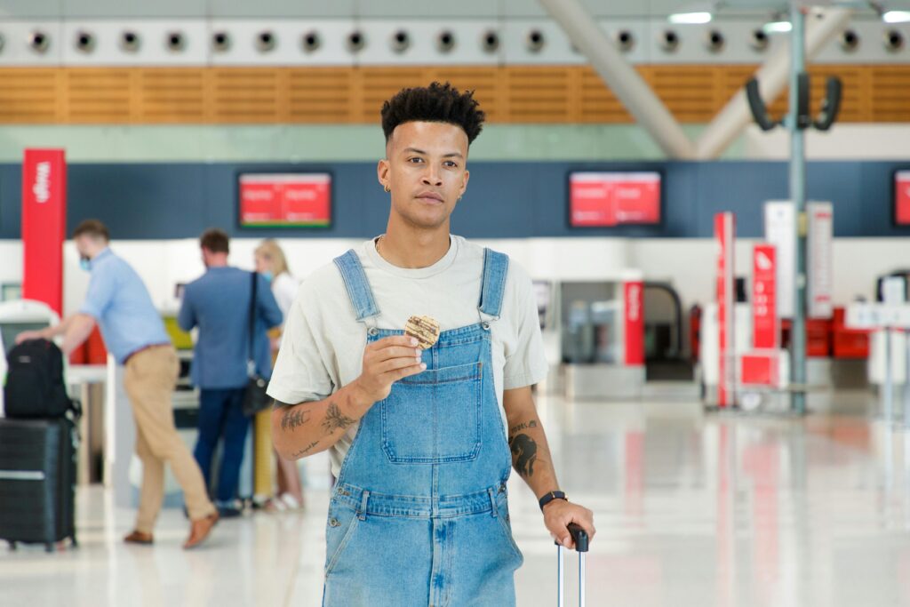 pexels-photo-12700185-12700185 Young man in denim jumper with cookie at airport terminal, ready to travel.